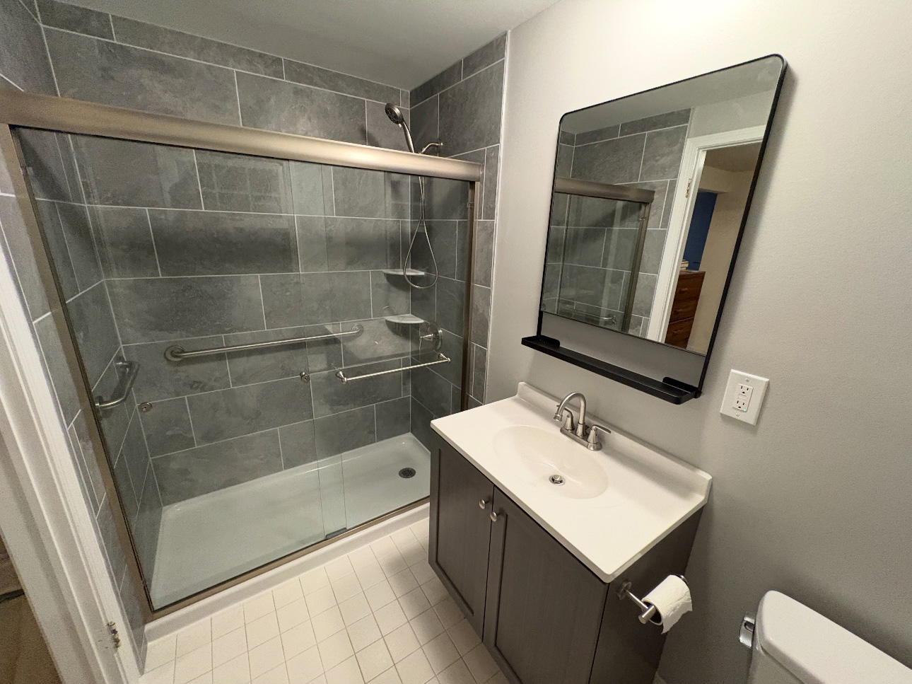Bathroom remodel with tub converted to walk-in shower, large gray tile surround, grab bars, and frameless sliding glass doors.
